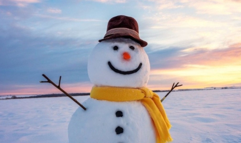 A picture of a snowman wearing a yellow scarf and a top hat in an open field covered in snow.